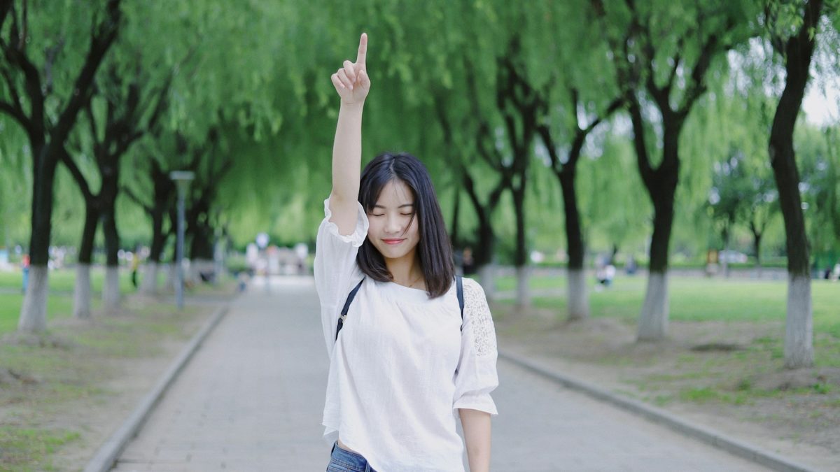 目を閉じて腕を上げて上を指す女性